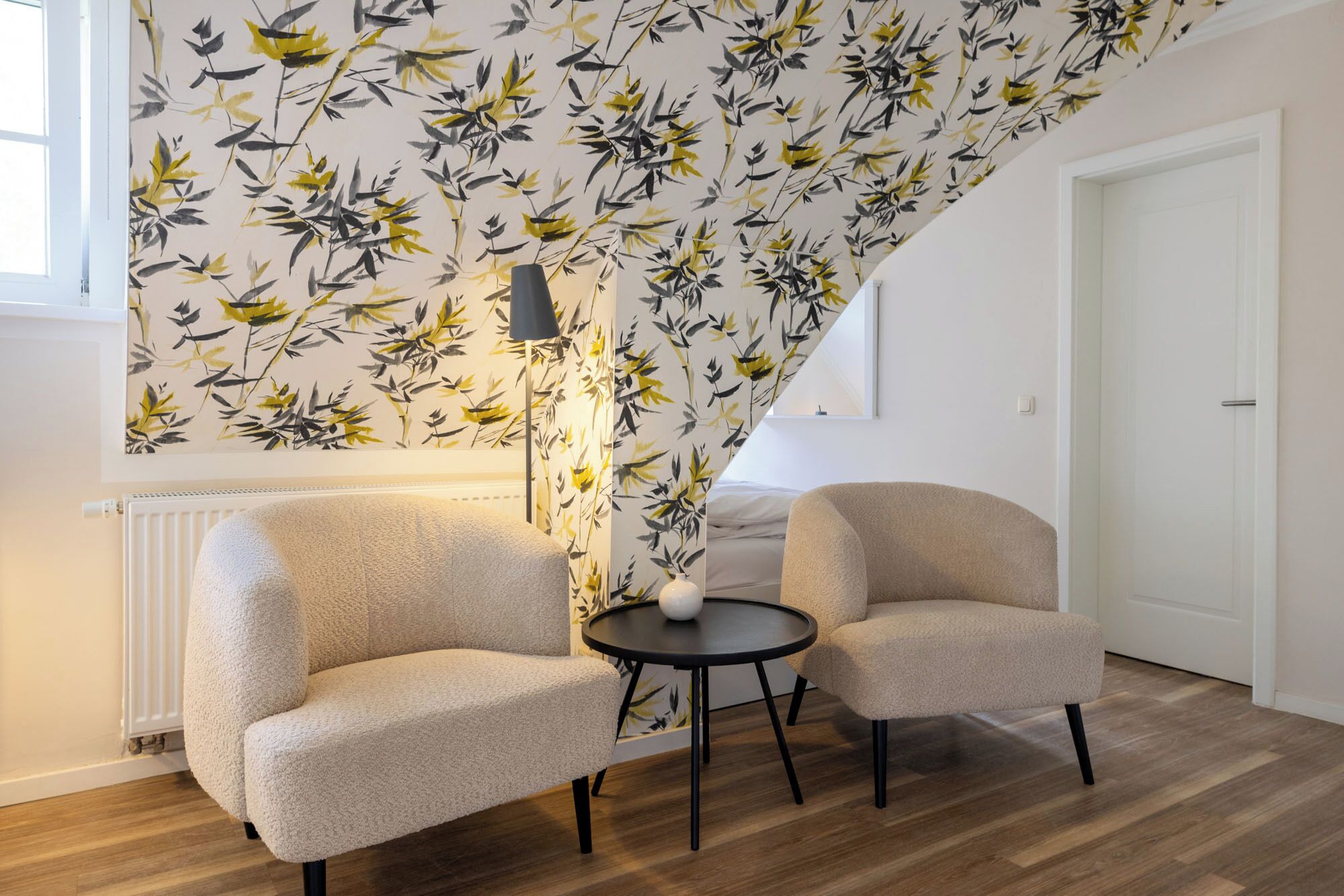 A room with a staircase, two armchairs, a small round table, and a radiator.
