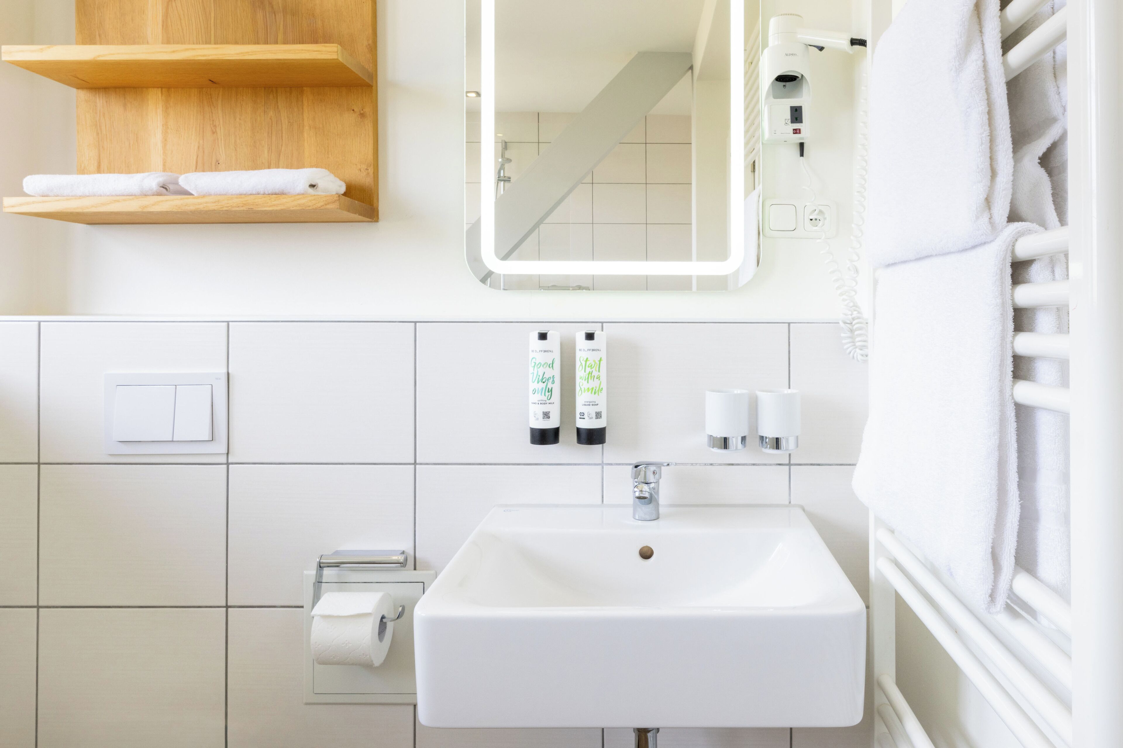 Une salle de bain avec un lavabo blanc, un miroir, un porte-serviettes et deux flacons de savon pour les mains.