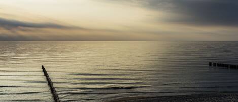 A beach with a wooden jetty extending into calm waters, under a cloudy sky.