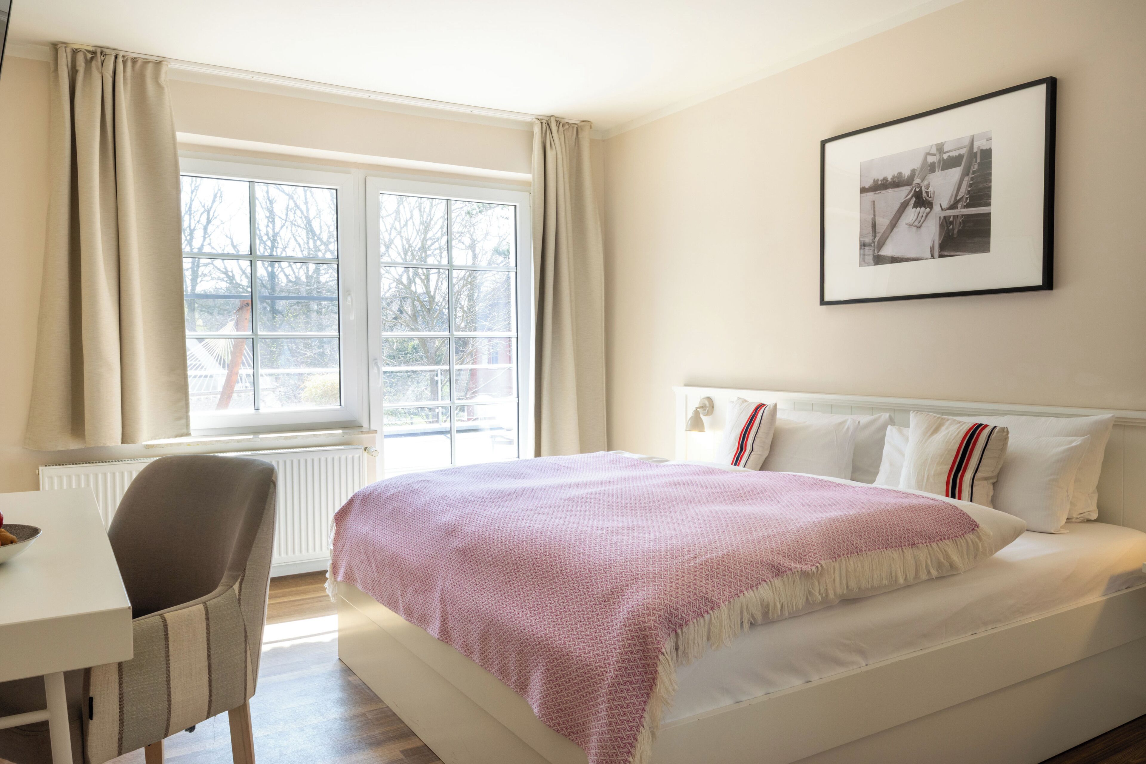 Un dormitorio con cama, una silla, un ventanal y un cuadro en la pared.