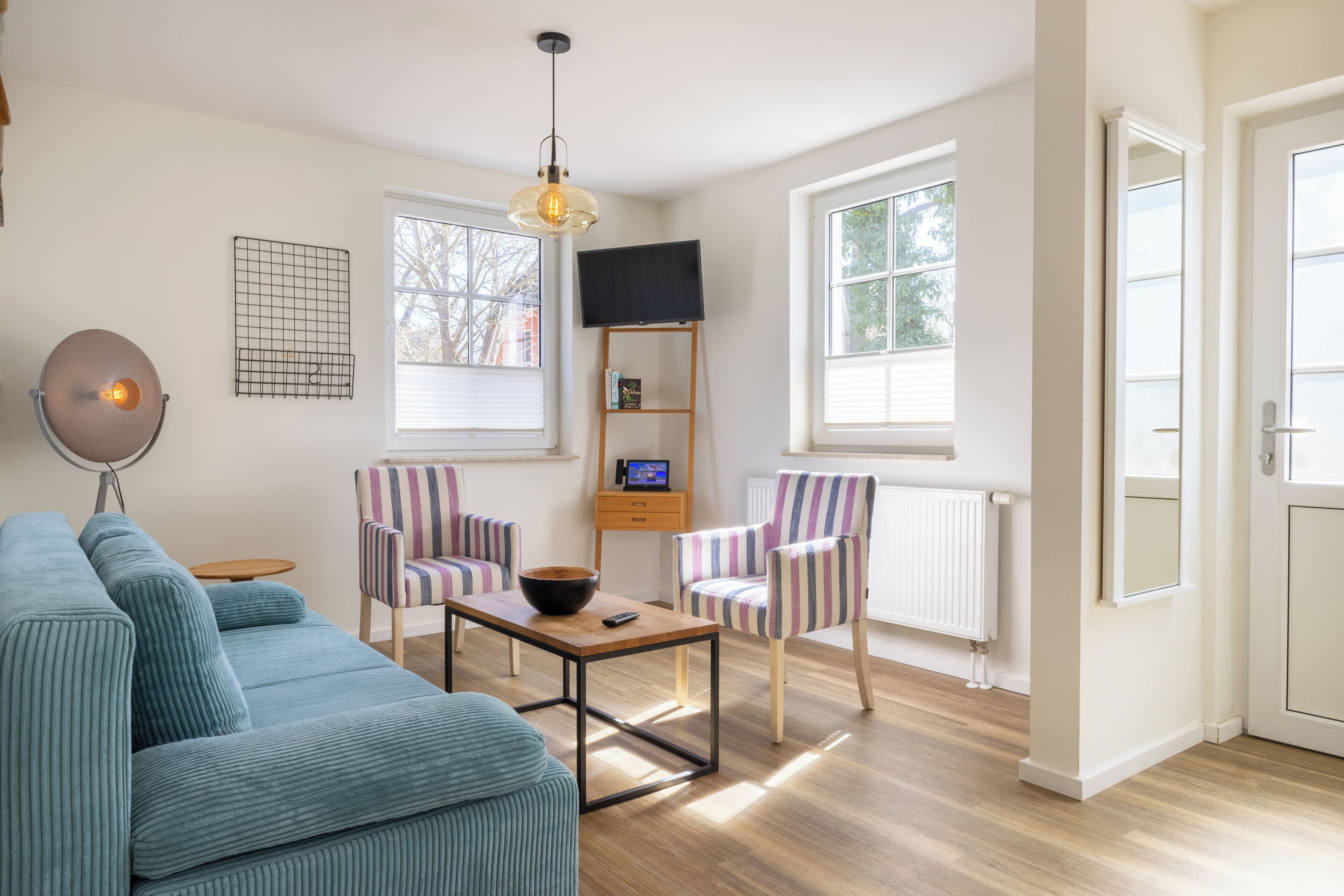 A living room with a sofa, two striped chairs, a coffee table, a TV on a stand, and a pendant light.