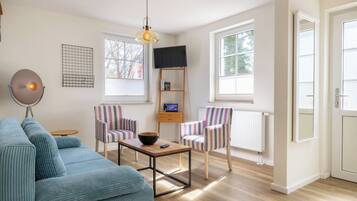 A living room with a sofa, two striped chairs, a coffee table, a TV on a stand, and a pendant light.