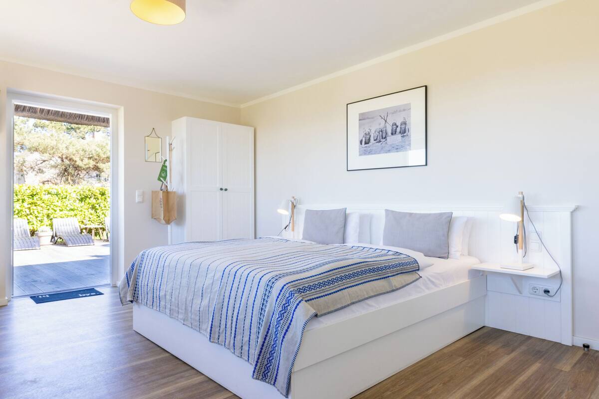 A bedroom with a bed, bedside tables, a framed picture, and a door leading to a balcony.