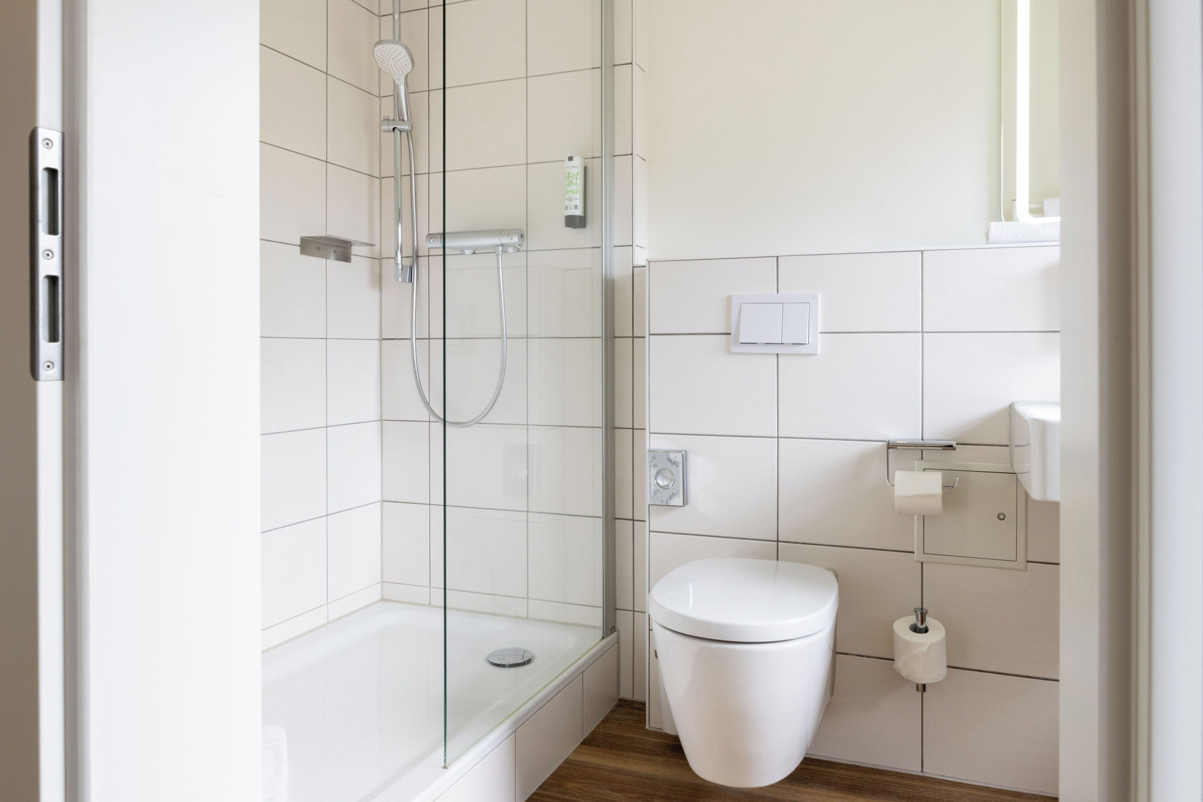 A modern bathroom with a glass-enclosed shower, a white toilet, and a tiled wall.