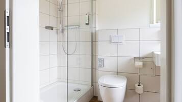 A modern bathroom with a glass-enclosed shower, a white toilet, and a tiled wall.