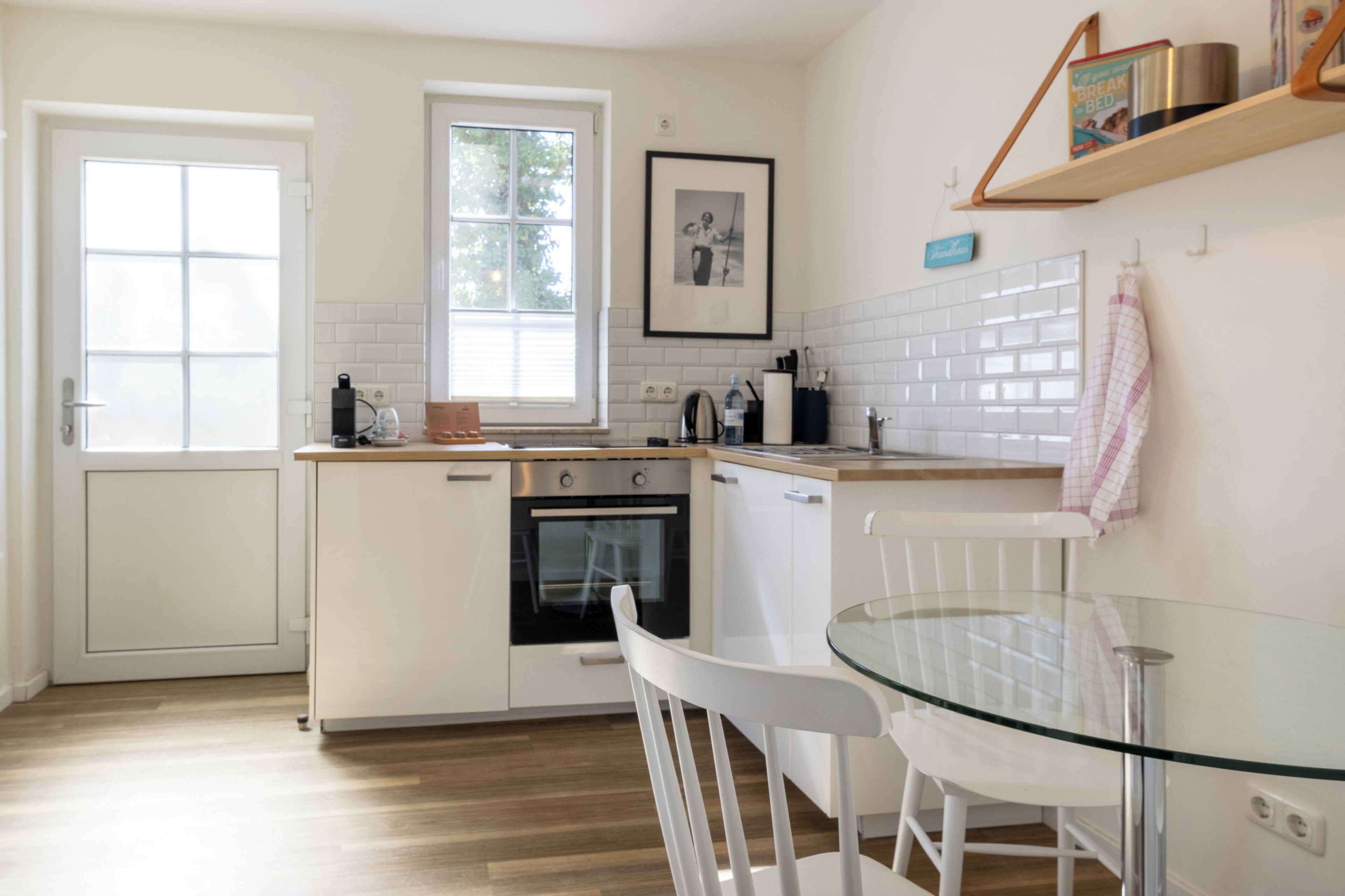Una cucina moderna con mobili bianchi, un tavolo in vetro e una finestra.