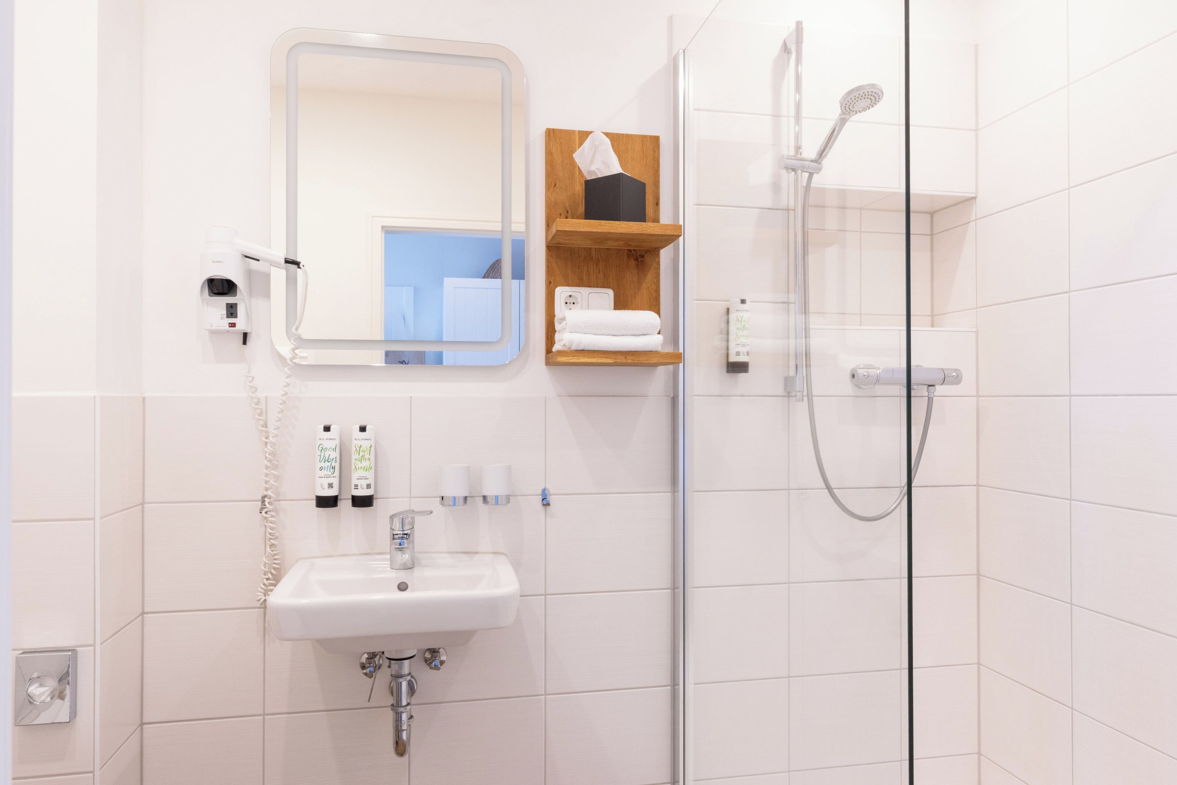 A modern bathroom with a sink, mirror, towel rack, and shower.