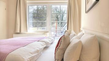 Un dormitorio con dos camas, una ventana con cortinas, un radiador y un cuadro en la pared.