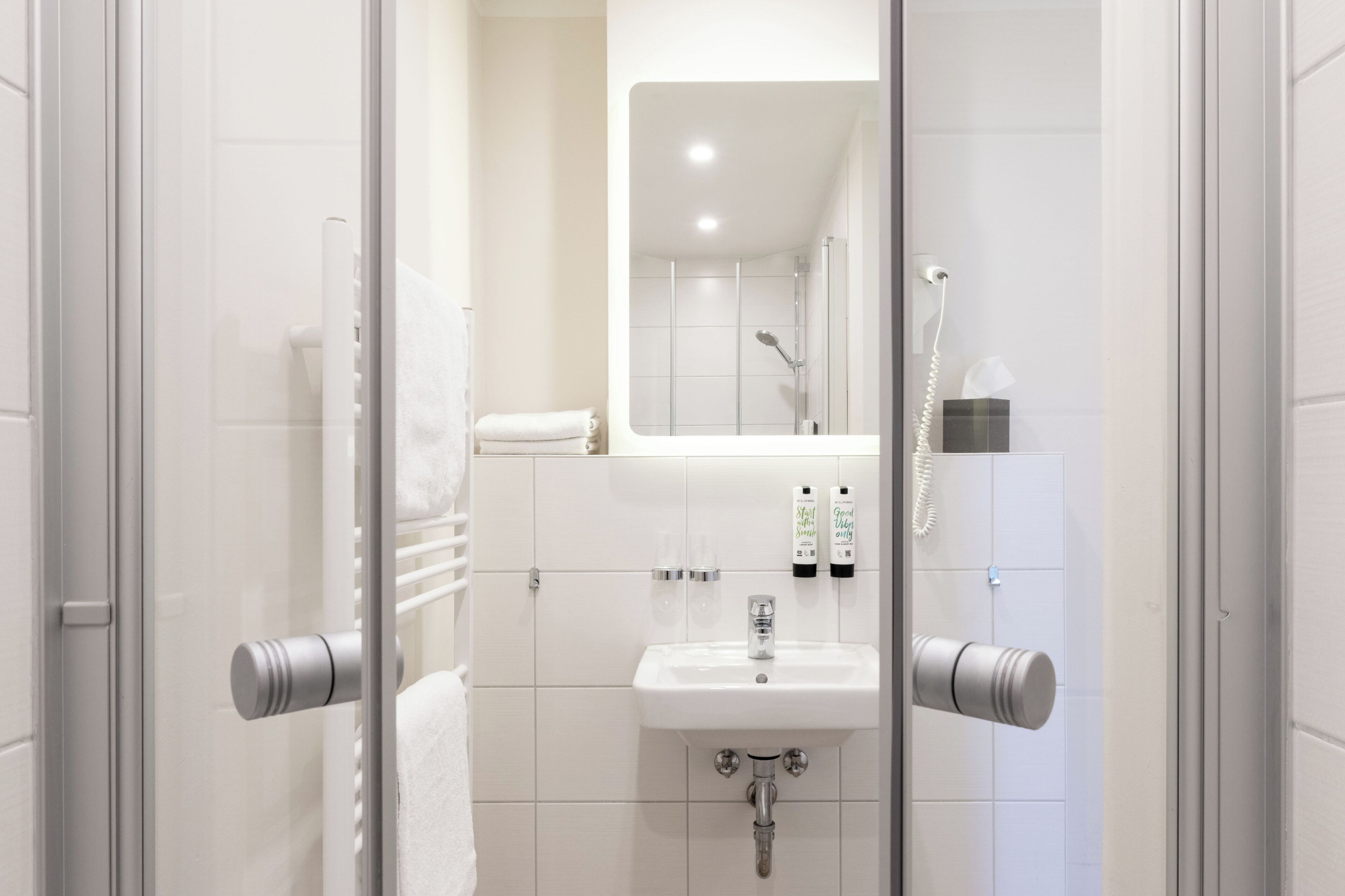 Ein modernes Badezimmer mit einer Duschkabine aus Glas, einem weißen Waschbecken und einem Spiegel darüber.