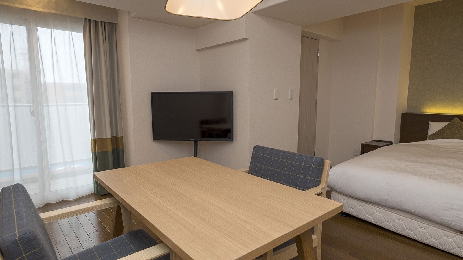 Una habitación de hotel con una mesa de madera, dos sillas, una cama, un televisor y una puerta.
