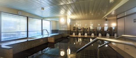 Un área de piscina interior moderna con suelo húmedo, un reloj en la pared y una hilera de lavamanos.