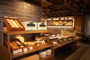 Un bufé de desayuno con diversos pasteles y pan, una estación de café y un área de descanso con mesas y sillas.