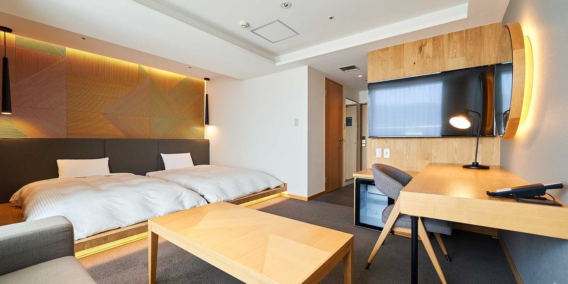 A hotel room with two beds, a desk, a chair, and a TV.