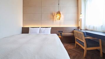 A hotel room with a large bed, a desk, a chair, a nightstand, and a wall-mounted lamp.