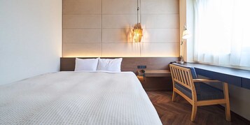 Una habitación de hotel con una cama grande, un escritorio, una silla, una mesita de noche y una lámpara de pared.