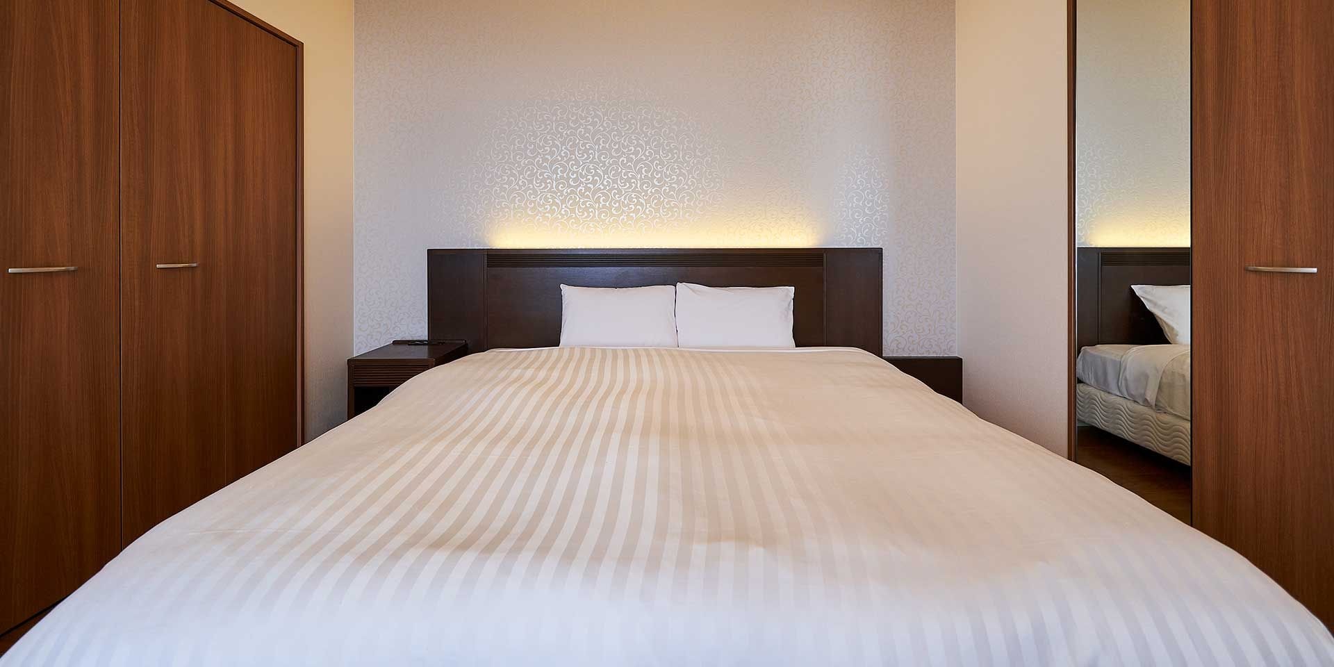 A hotel room with a large bed, a nightstand, a headboard with a light, and wooden wardrobes.