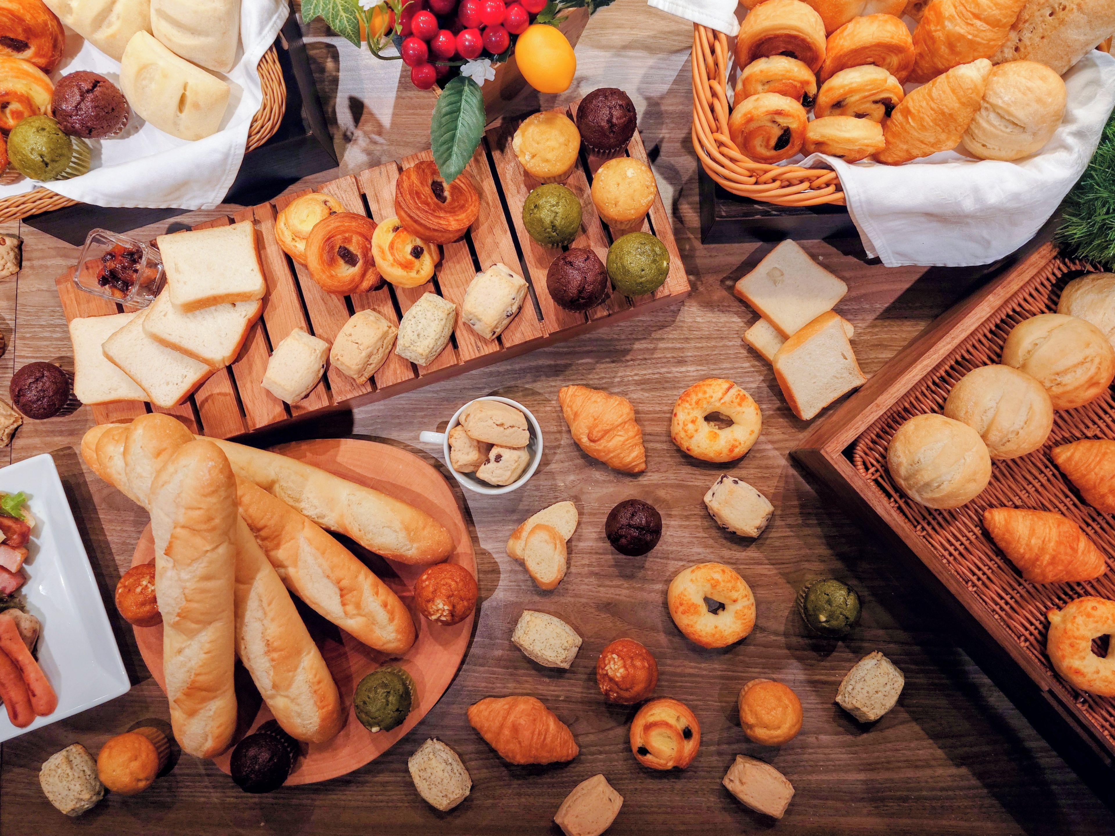 A variety of baked goods including bread, pastries, and muffins arranged on wooden surfaces.