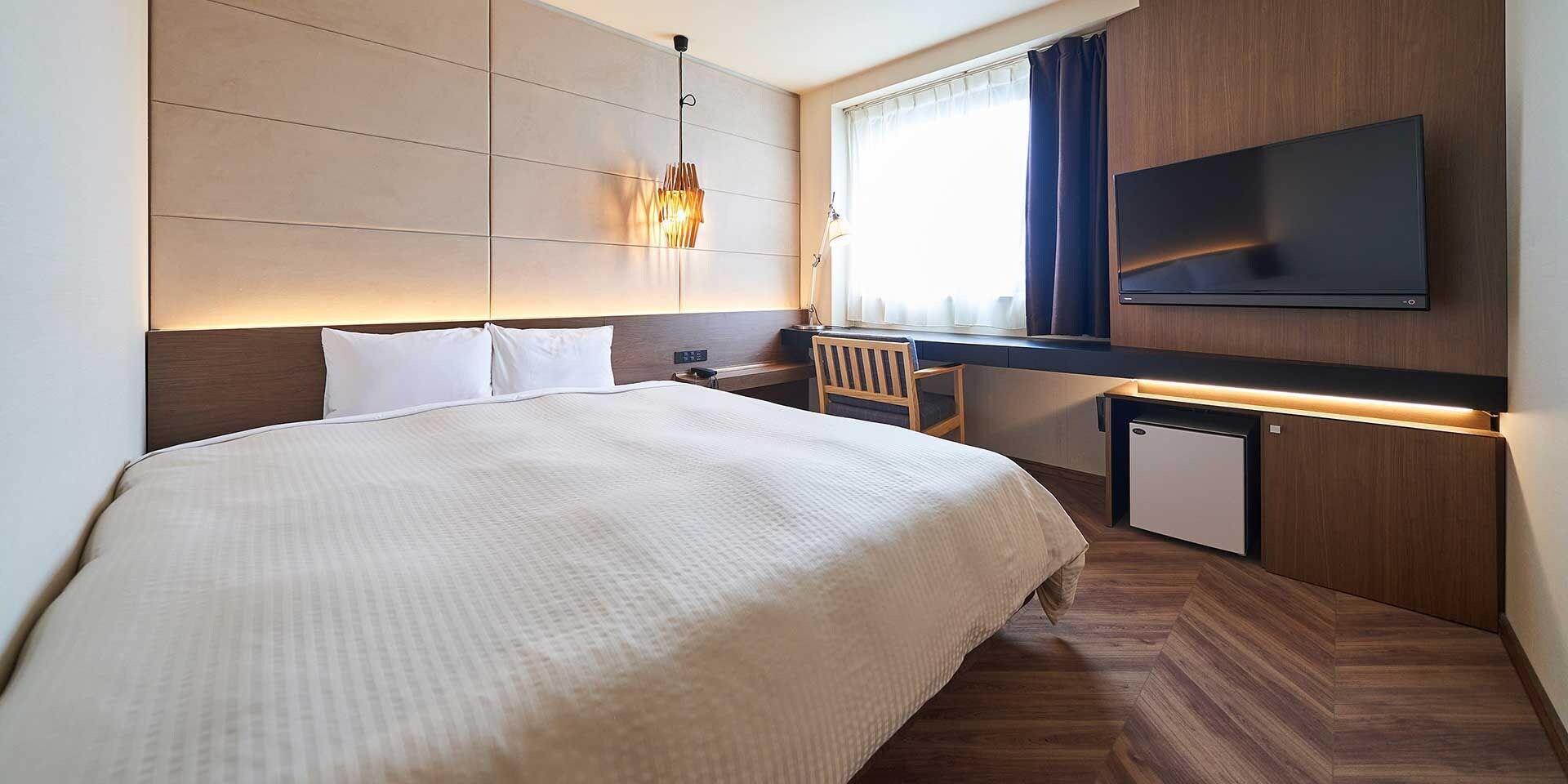 A hotel room with a bed, bedside table, lamp, TV, and a small cabinet.