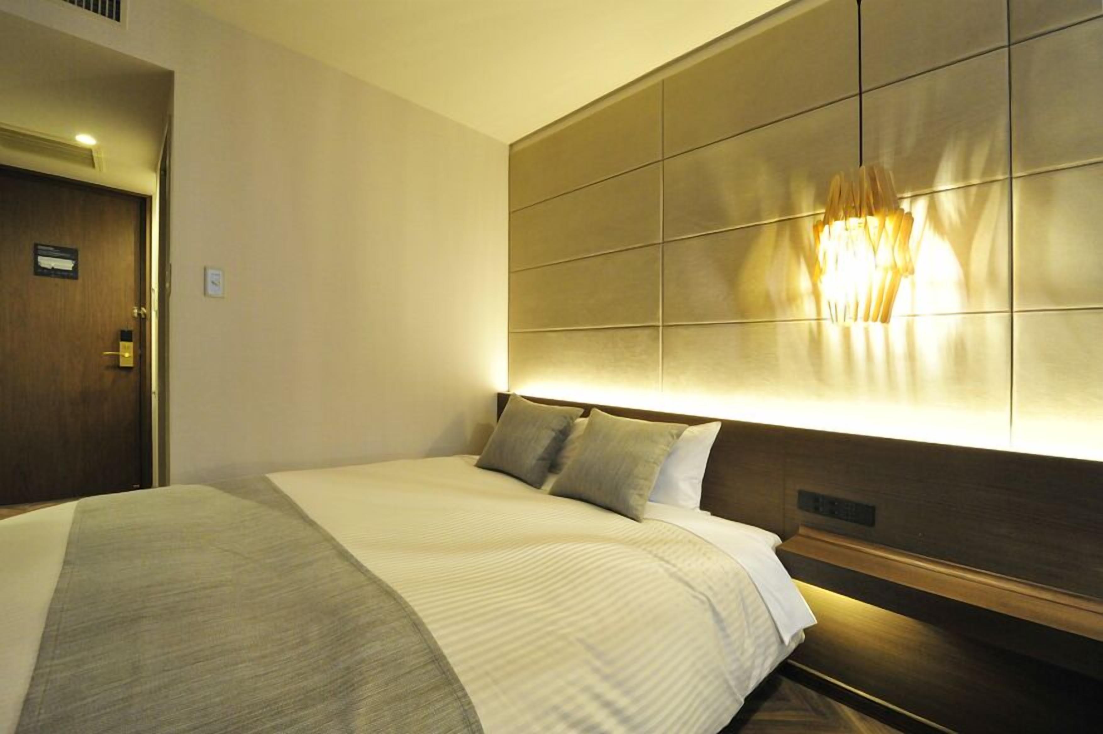 Ett hotellrum med en stor säng, en sänggavel med en lampa och en dörr med en skylt.
