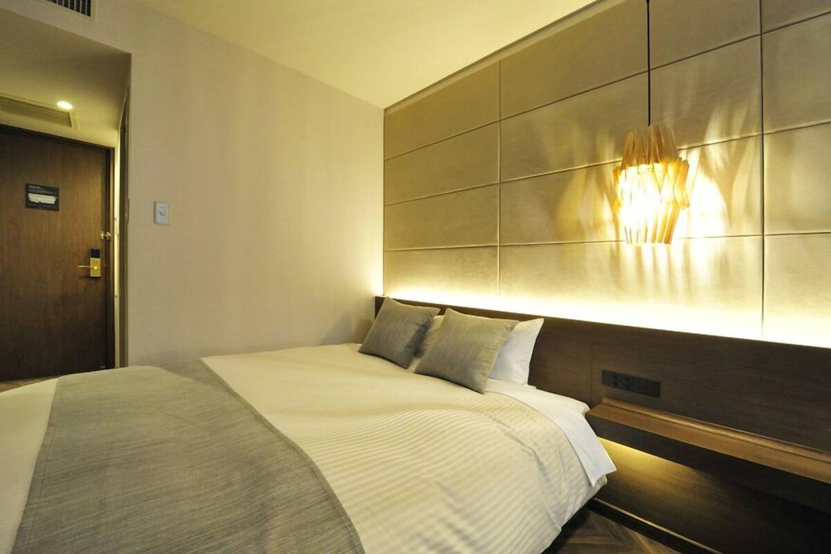 A hotel room with a large bed, a headboard with a light fixture, and a door with a sign.