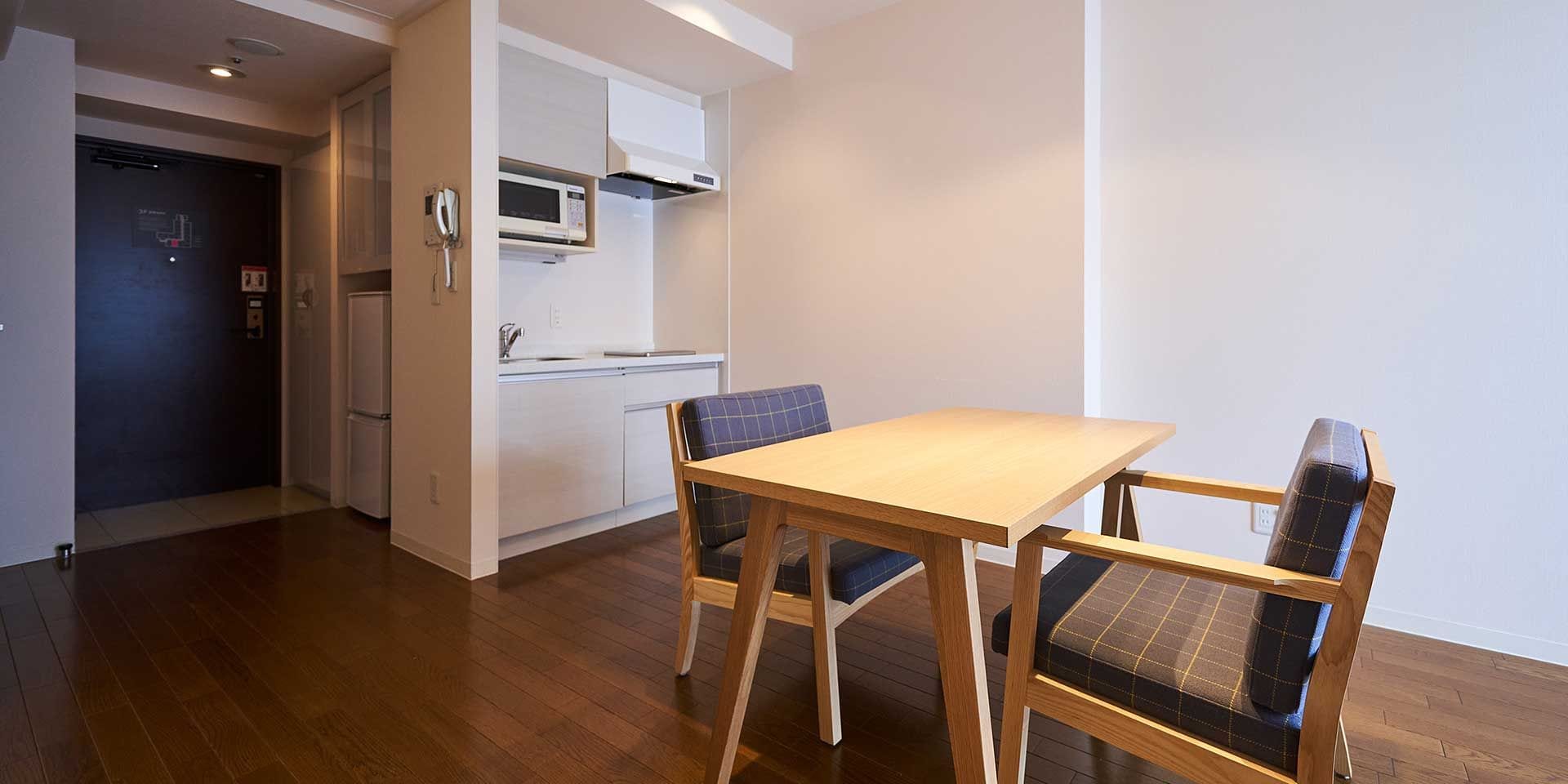 A compact kitchen with a microwave, a refrigerator, and a sink. There is a wooden table with two chairs.