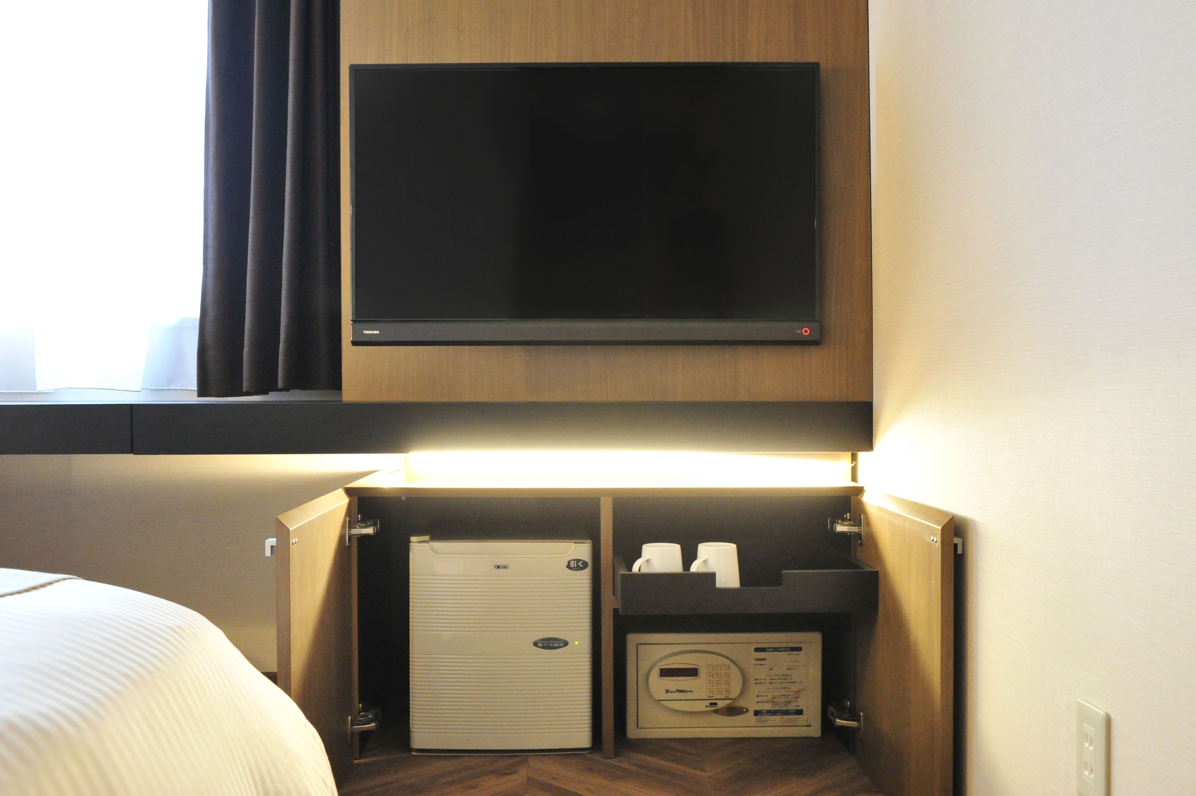 A hotel room with a bed, a television mounted on a wooden cabinet, a minibar, and a coffee machine.