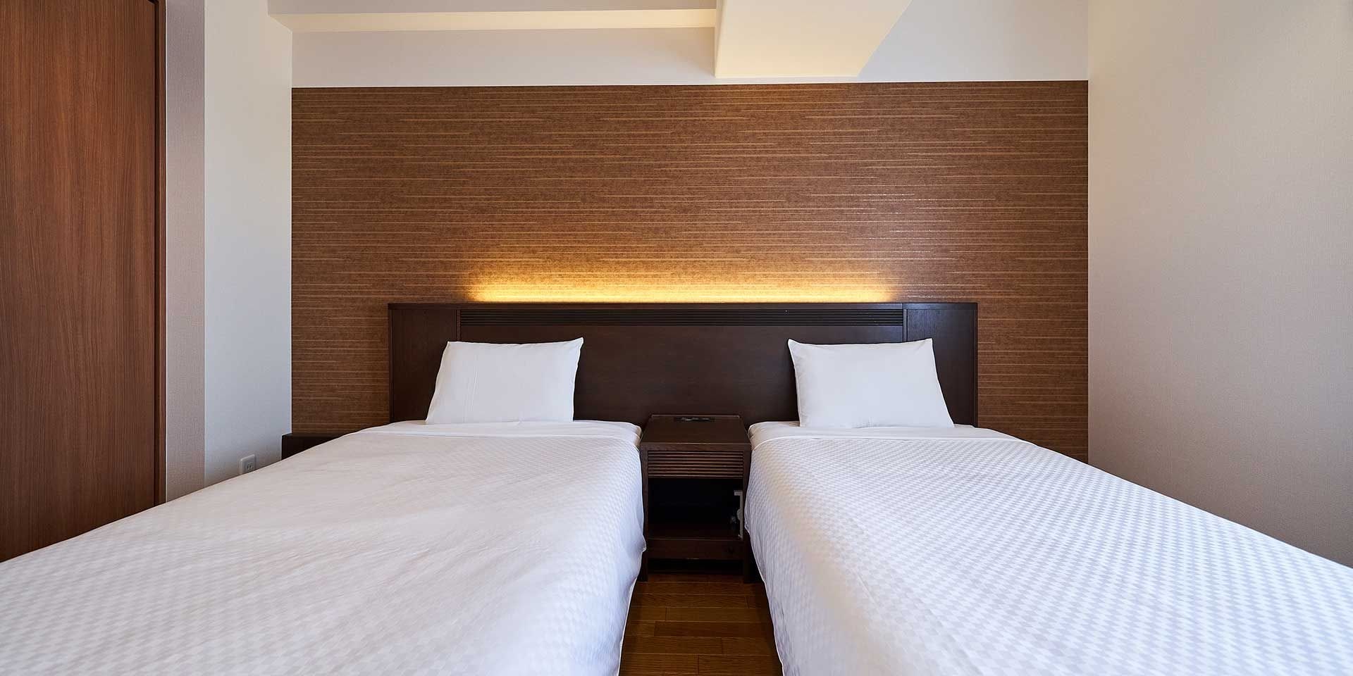 Una habitación de hotel con dos camas individuales, un cabecero de madera y una mesita de noche entre ellas.