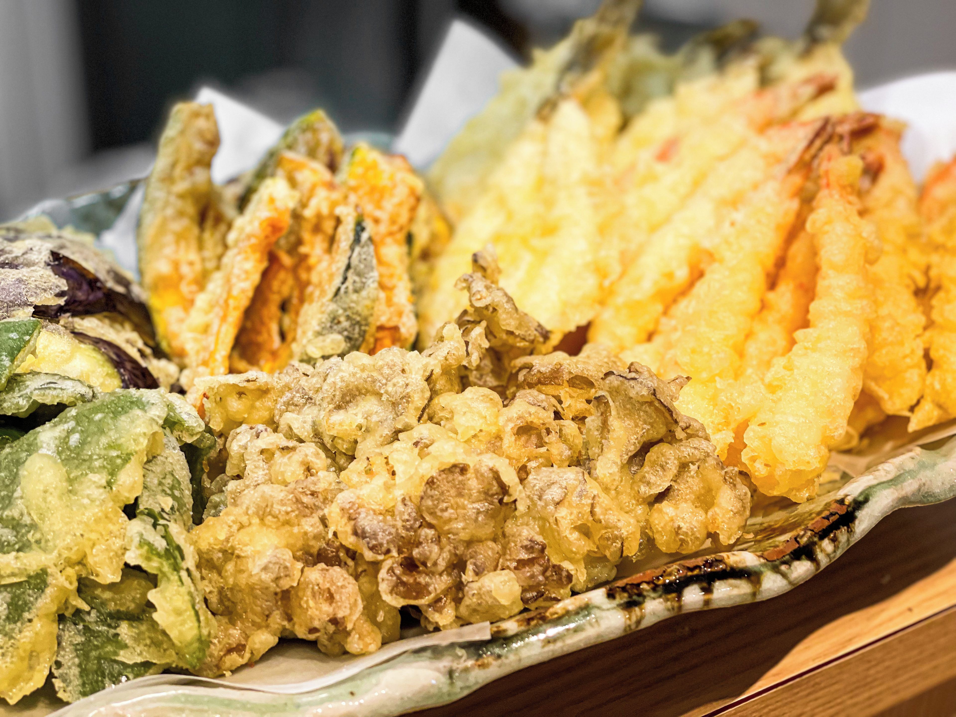 A variety of fried foods, including tempura and possibly okonomiyaki, served on a ceramic plate.