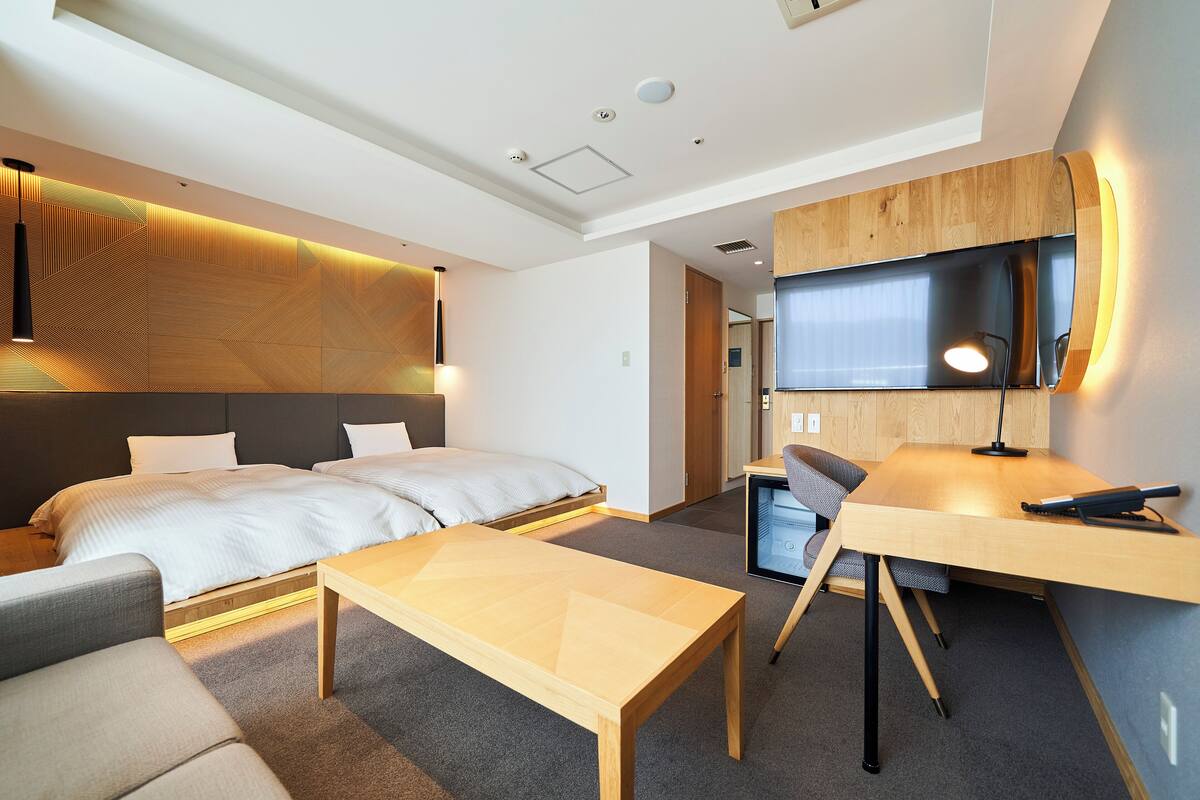 A modern hotel room with a bed, a desk, a chair, and a sofa.