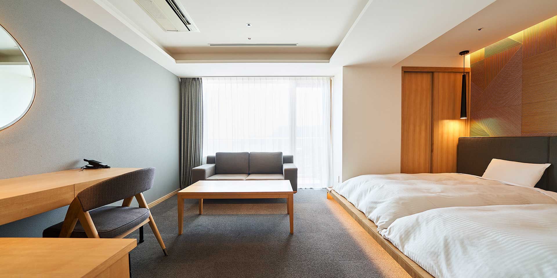 Habitación de hotel con cama, escritorio, sofá y un amplio ventanal con cortinas.