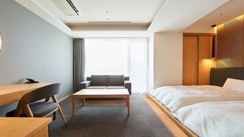 Habitación de hotel con cama, escritorio, sofá y un amplio ventanal con cortinas.