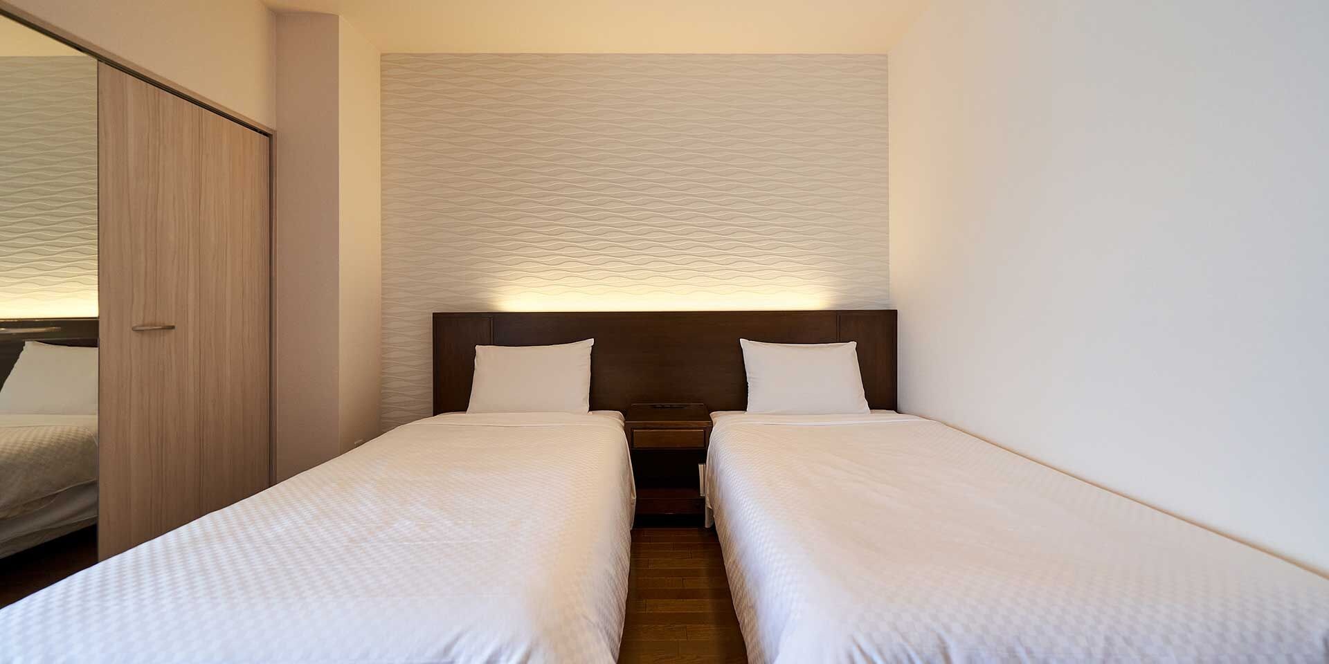 A hotel room with two single beds, a wooden wardrobe, and a textured wall.