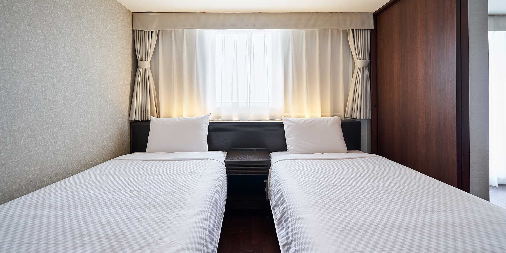 Habitación de hotel con dos camas, cabecera y ventana con cortinas.