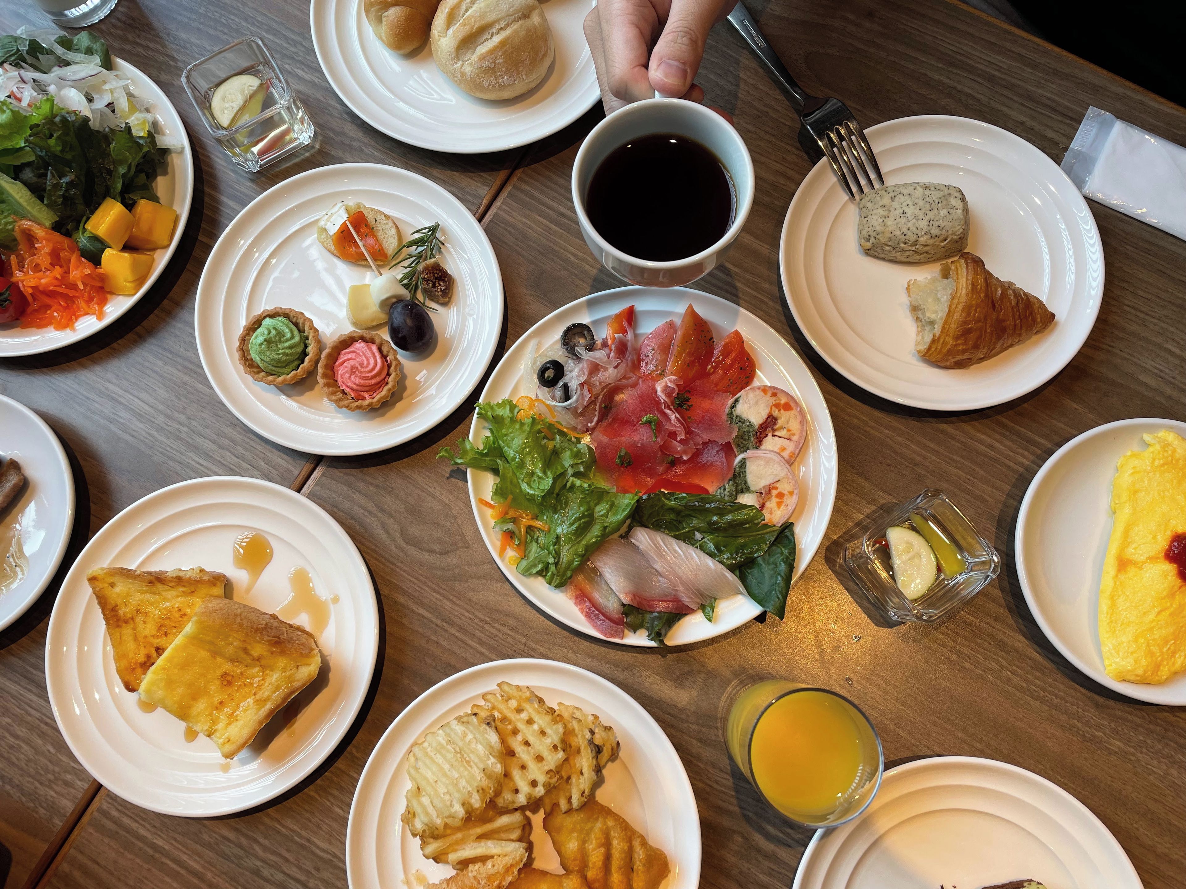 A variety of dishes on a table, including salads, pastries, and a plate with smoked salmon and prosciutto.