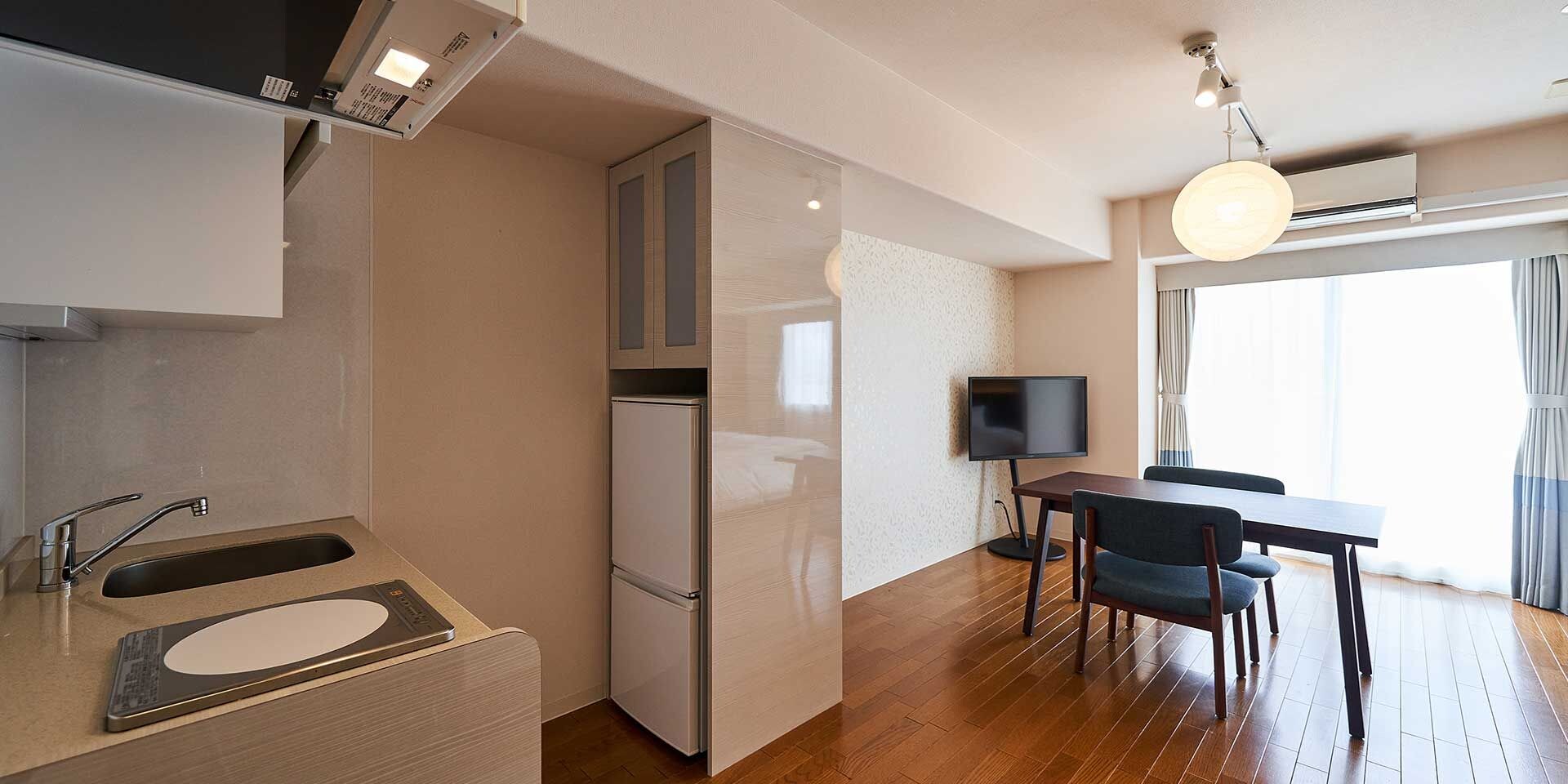 Cocina compacta con refrigerador integrado, zona de comedor con mesa y sillas, y un televisor.