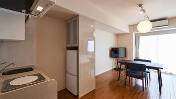 Cocina compacta con refrigerador integrado, zona de comedor con mesa y sillas, y un televisor.