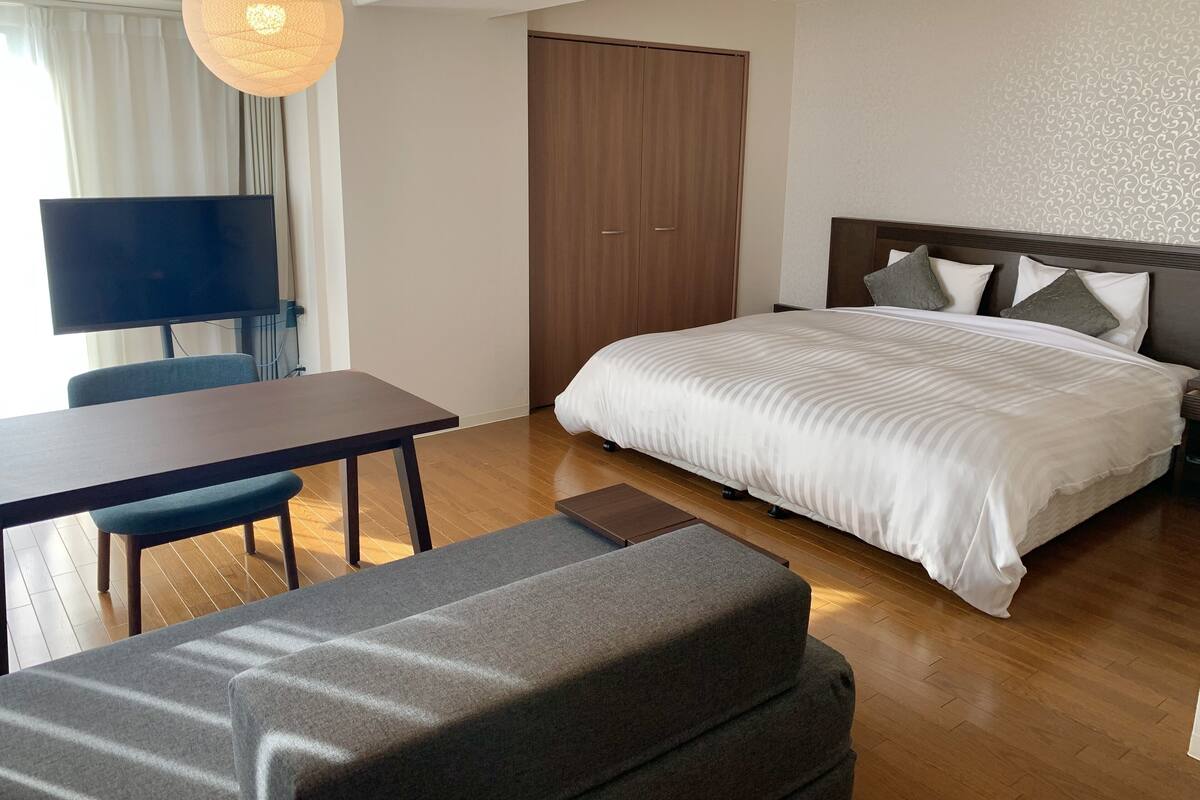 A modern bedroom with a large bed, a desk, a chair, and a television.
