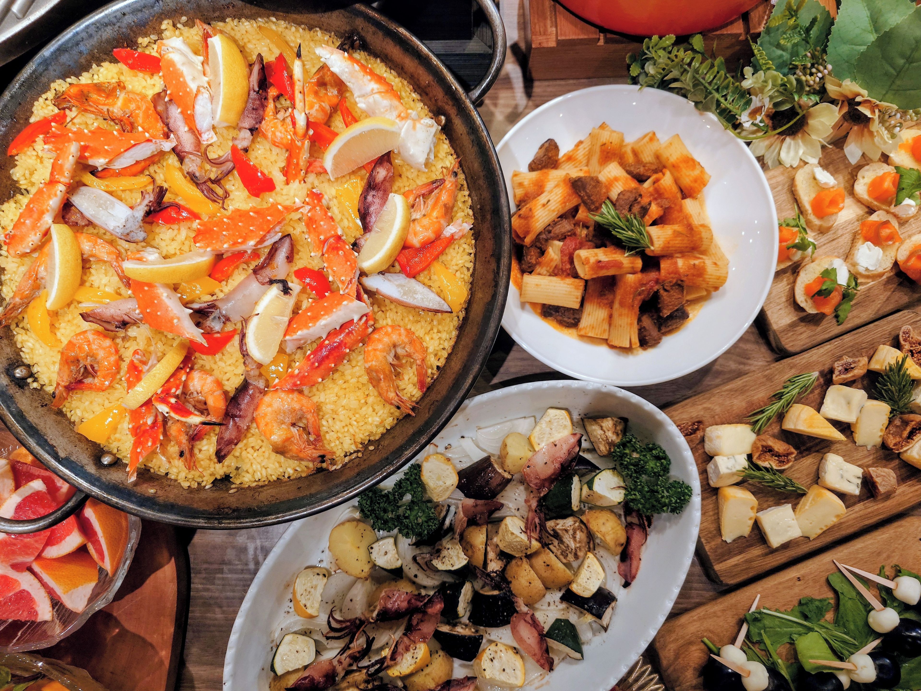 Diversos platos, como paella de mariscos, pasta con carne y brochetas de queso y verduras.