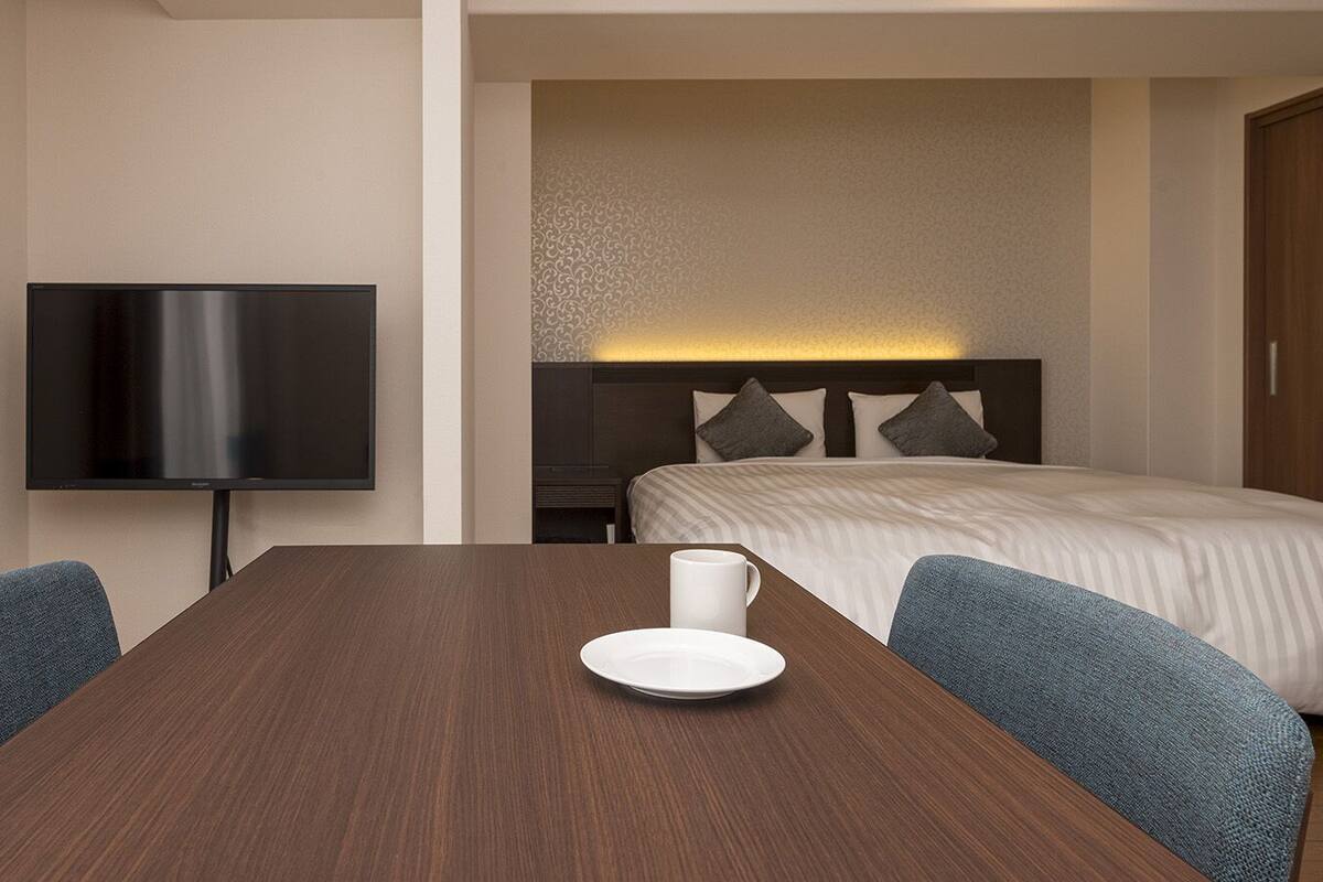 A hotel room with a bed, a TV, and a dining table with chairs.