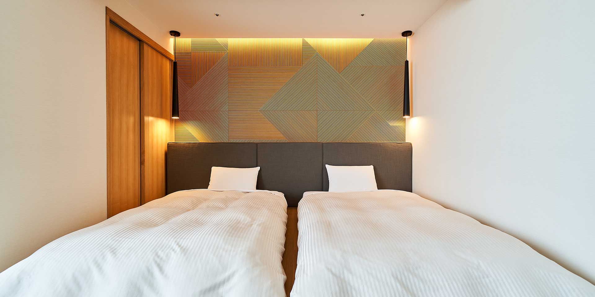 Habitación de hotel con dos camas, un armario de madera y una pared con diseño geométrico.