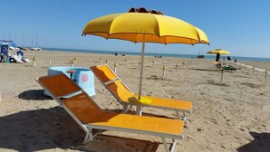 A beach with sun loungers and yellow umbrellas. - Hotel Nova Dhely (Rimini)
