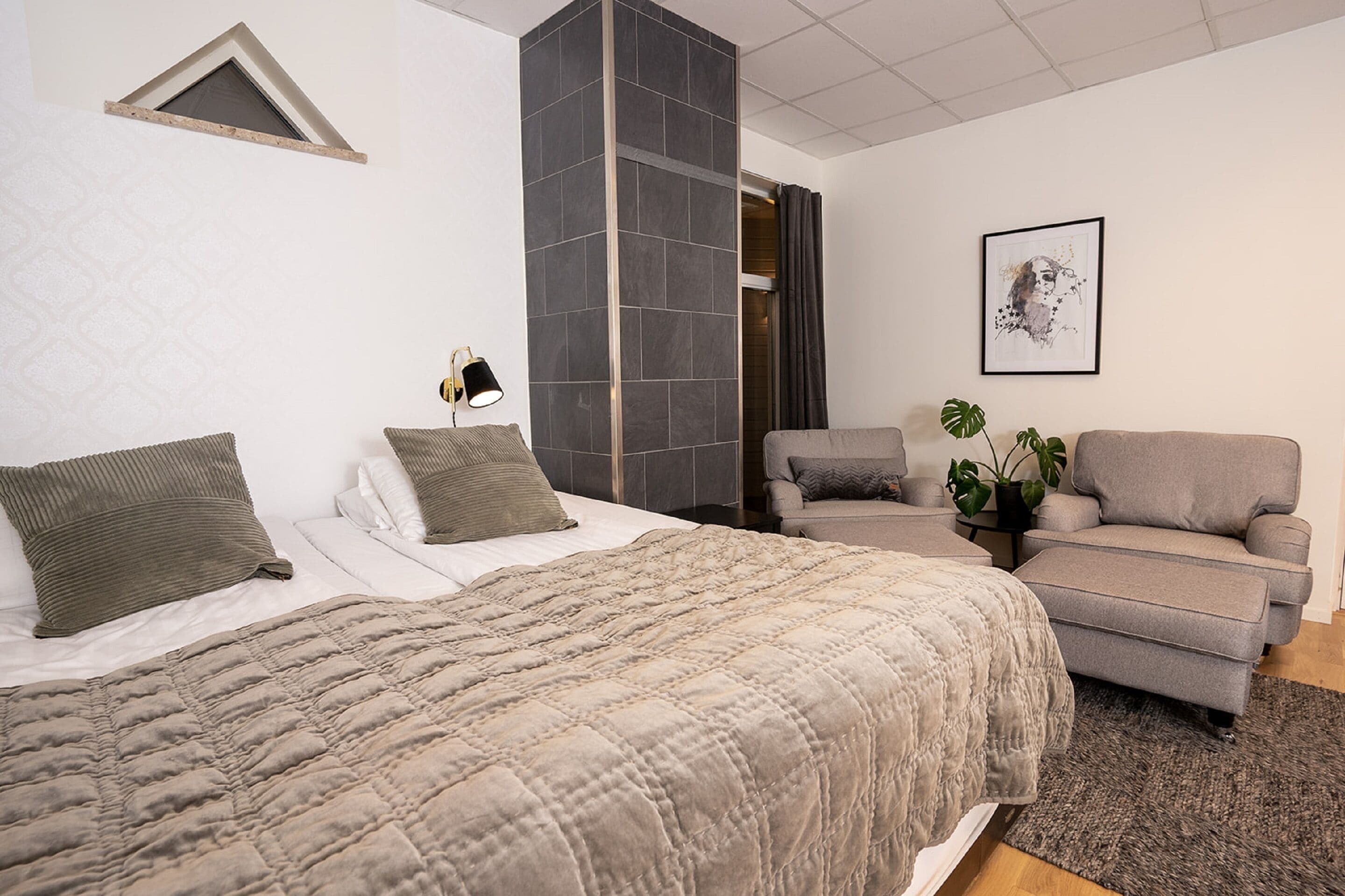 Une chambre moderne avec un grand lit, un canapé, une petite table avec une lampe et une plante en pot.