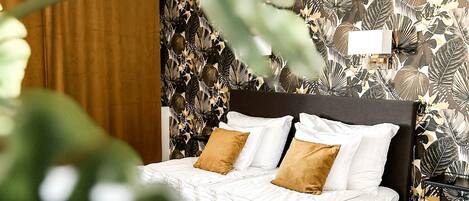 Un dormitorio con cama, suelo de madera y una pared con diseño de hojas.