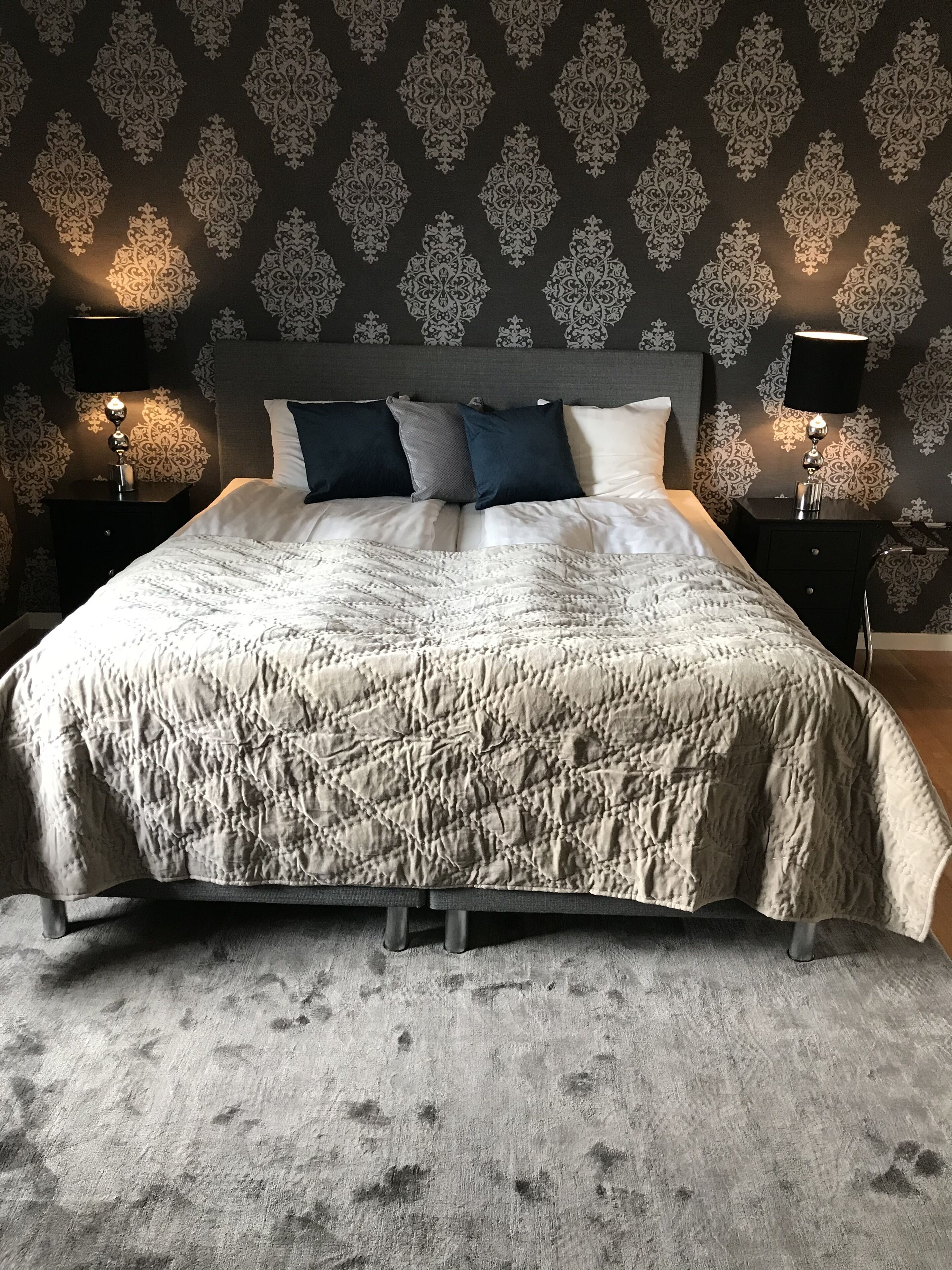 A bed with a textured quilt, two bedside tables with lamps, and a patterned wallpaper.