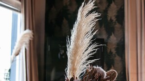 A vase with dried flowers on a table in a room with a sofa and curtains. - Hotell Ronja (Vimmerby)