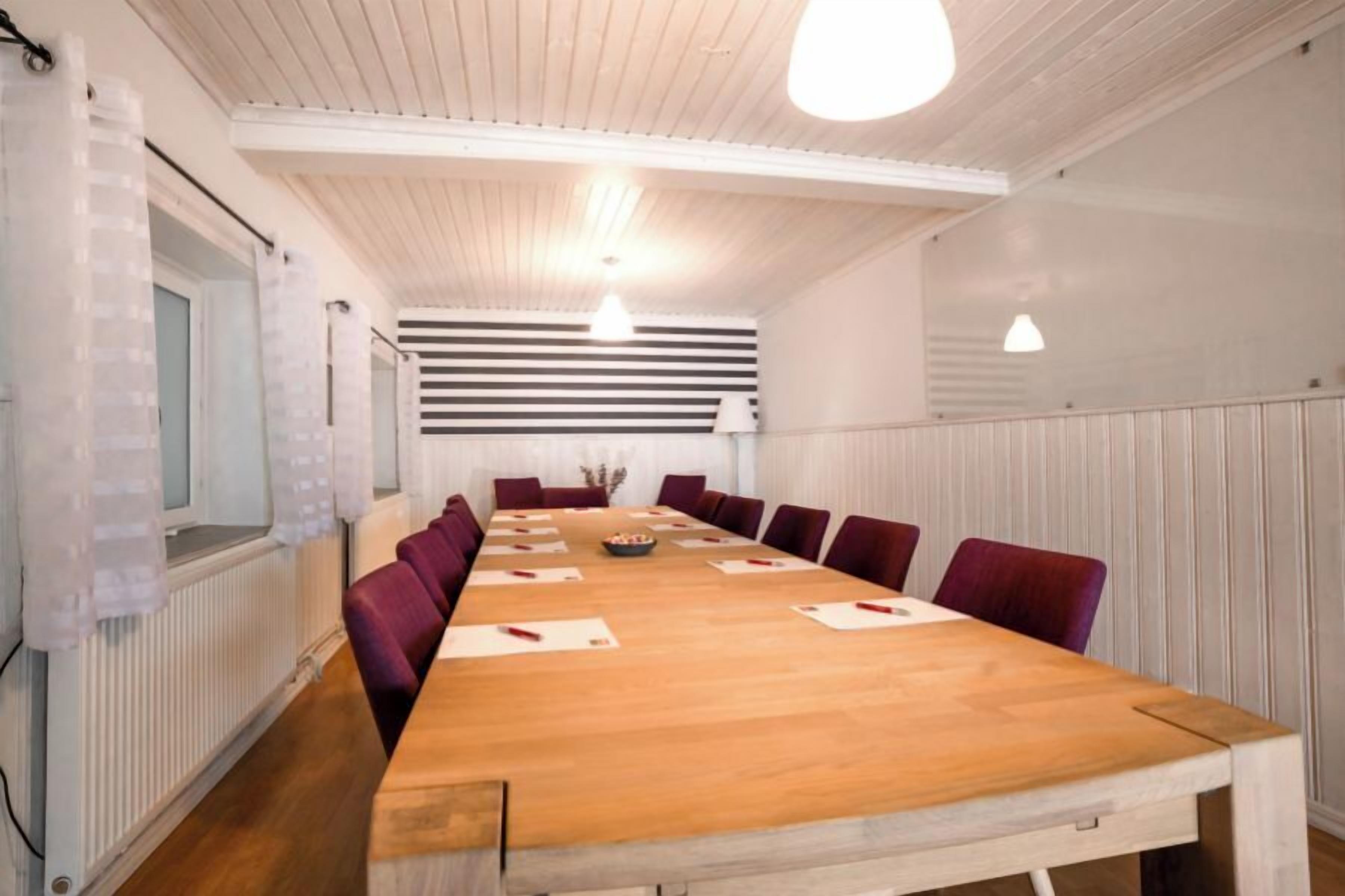 A conference room with a long wooden table, purple chairs, and a white ceiling with a light fixture.