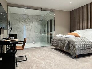 A modern bedroom with a glass shower, a bed with a quilted duvet, and a desk with a chair. - Hotell Ronja (Vimmerby)