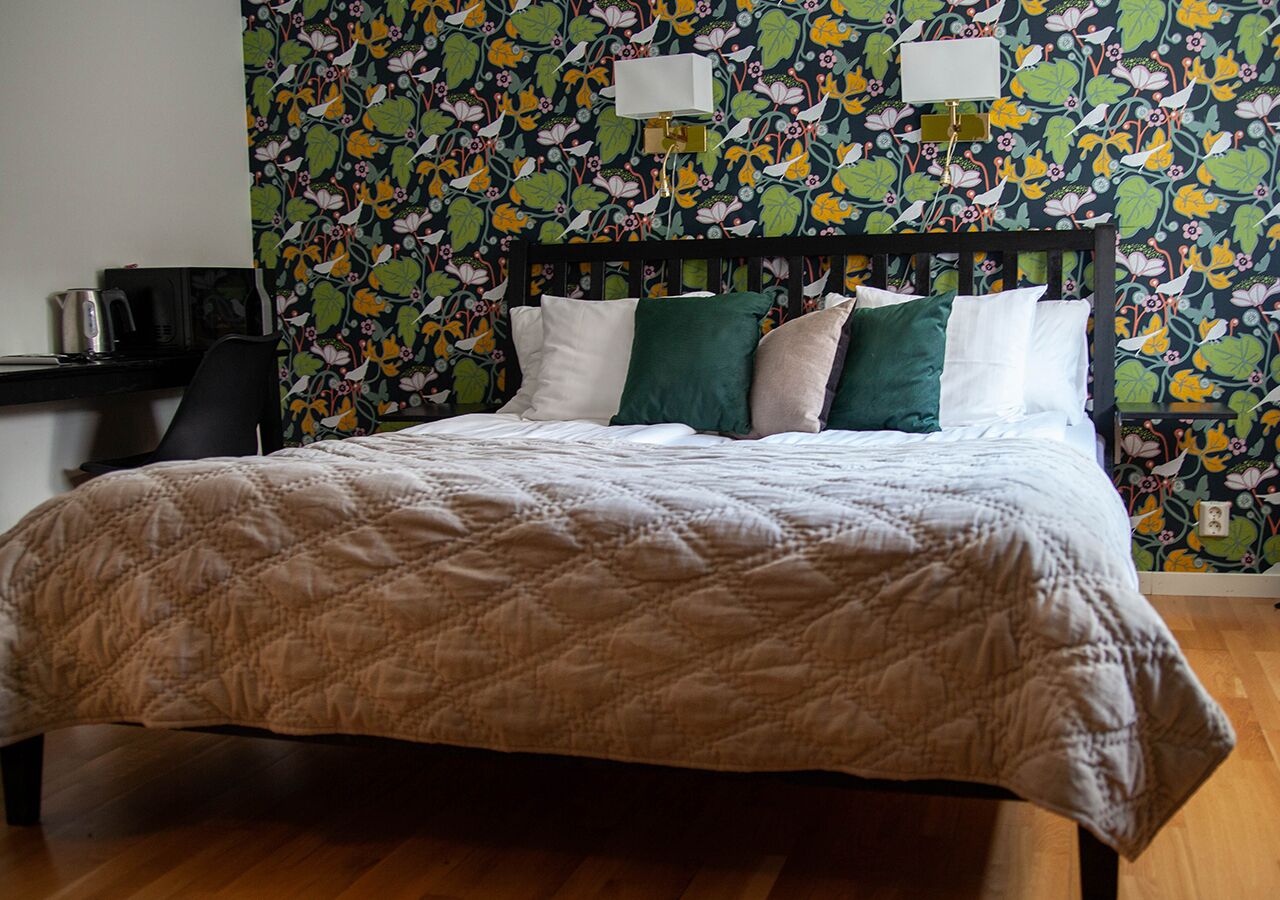 A bed with a quilted bedspread, a wooden headboard, and a floral wallpaper pattern.