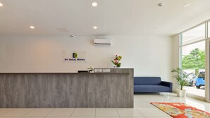 Zona de recepción de hotel con un mostrador gris, un sofá azul y un ventanal con vistas al exterior.