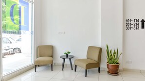 Un hall de hotel con dos sillones color beige, una mesita redonda con una planta y un ventanal con vista a coches estacionados.